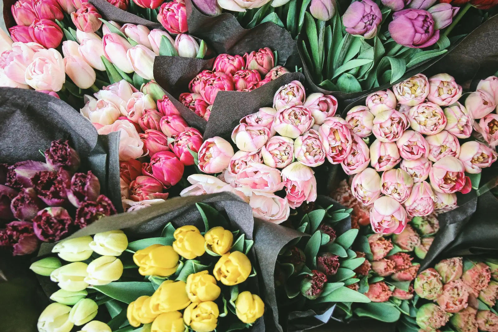 Bunches of pink, yellow and white tulips and peonies wrapped in paper, packed together and seen from above